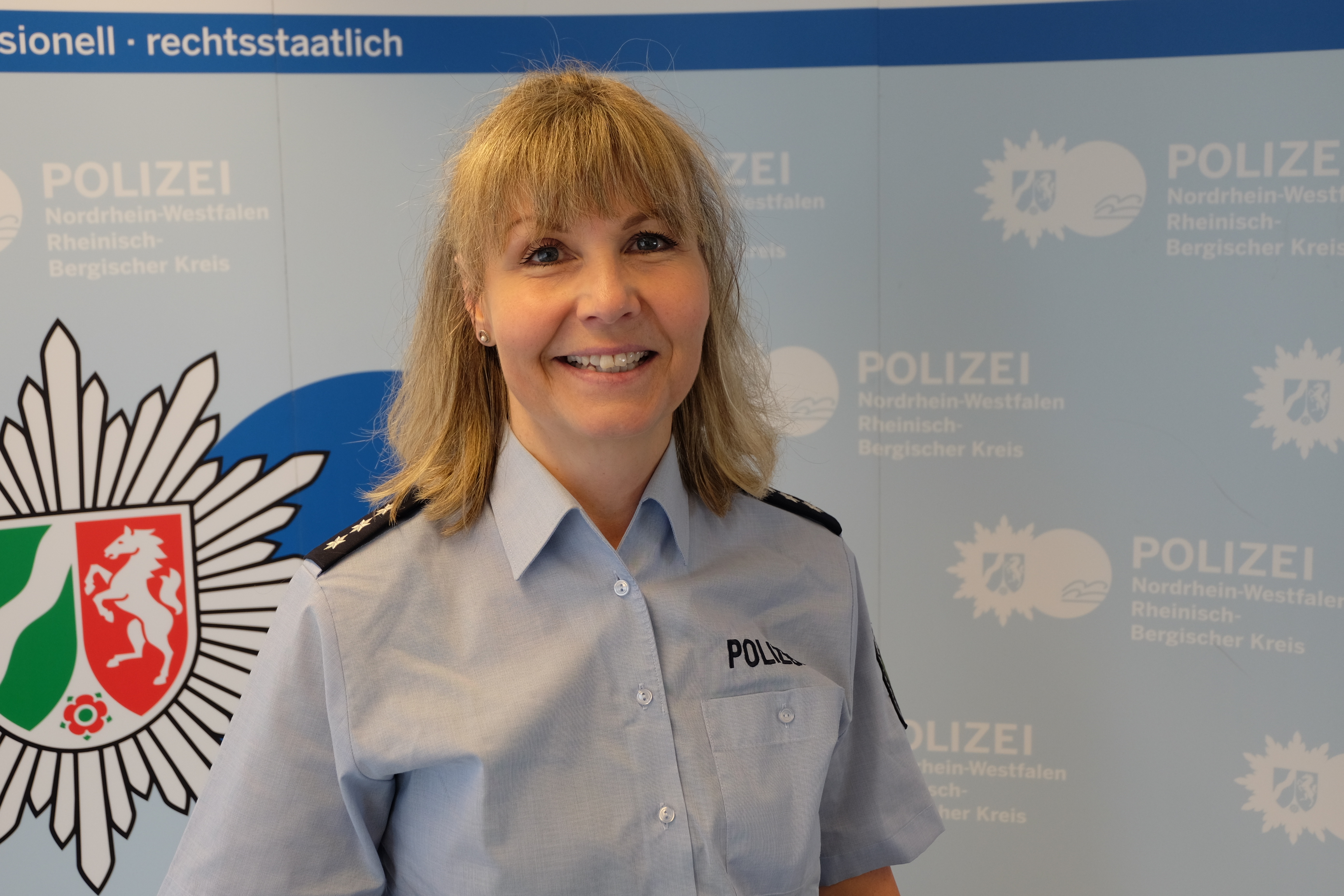 Portrait der Polizeihauptkommissarin Neuhausen vor der Presseleinwand