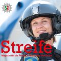 Eine Polizistin der Fliegerstaffel seilt sich von einem Hubschrauber ab. Sie trägt Uniform und Helm. Auf dem Oberarm ist das Wappen der Polizeifliegerstaffel zu sehen. Sie lächelt.