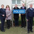 Personengruppe vor dem Polizeigebäude Oelde, aufgestellt um ein blaues Schild mit dem Aufdruck Polizei